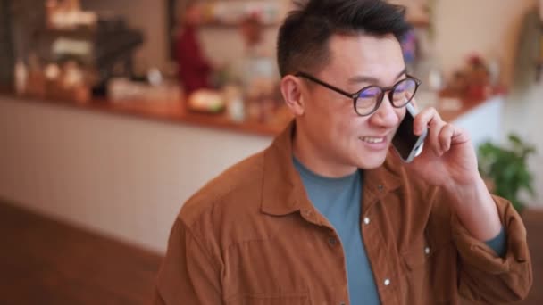 Riéndose Joven Asiático Con Gafas Hablando Por Teléfono Cafetería — Vídeo de stock