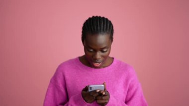 Pembe stüdyoda telefonla mesajlaşan güzel Afrikalı kadın.