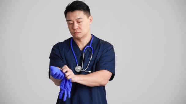 Pewny Siebie Azjatycki Lekarz Zakładający Rękawiczki Szarym Studio — Wideo stockowe