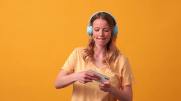 Blond Kvinna Bär Gul Shirt Spela Spel Telefon Hörlurar Orange — Stockvideo
