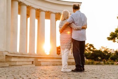 Beyaz yaşlı çift sarılıyor ve gün batımını seyrediyor.