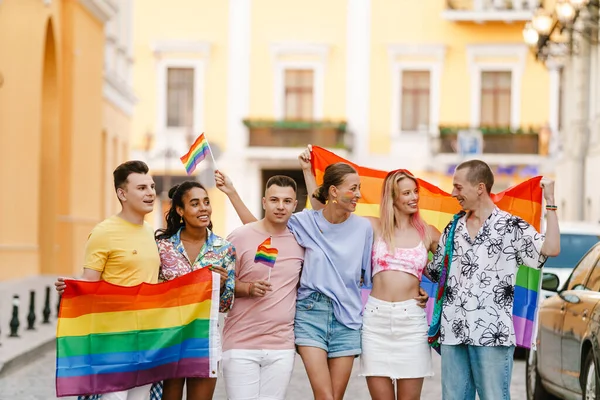 Şehir caddesindeki geçit töreninde gökkuşağı bayraklarıyla yürüyen çok ırklı erkek ve kadınlar.