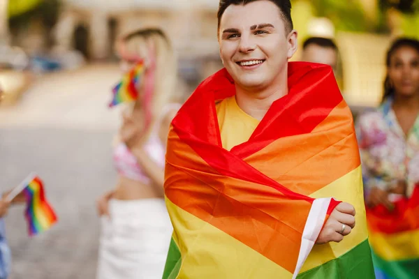 路上を歩いているLgbtコミュニティのパレードに笑顔の異なる人々のグループの間で立って虹の旗を保持笑顔の若い男の閉じる — ストック写真