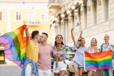 Bir grup gülen insan, lgbt topluluğunun geçit töreninde sokakta yürüyor.