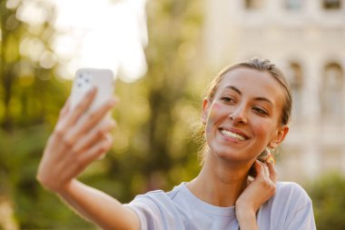 Gurur yürüyüşü sırasında sokakta ayakta duran ve selfie çeken neşeli genç bir kadın.