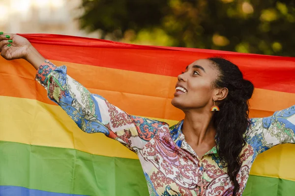 街の通りでプライドパレード中に黒の女性が笑顔と虹の旗を保持 — ストック写真
