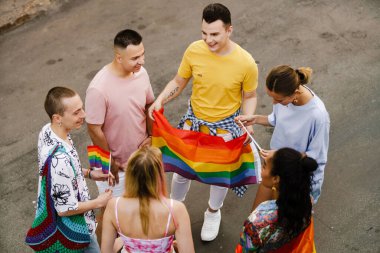 Şehrin sokaklarında geçit töreninde gülümseyen ve gökkuşağı bayrakları tutan genç gayler.