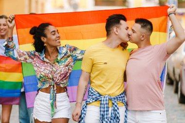 Şehrin sokaklarında geçit töreninde öpüşen ve gökkuşağı bayrağı tutan genç eşcinseller