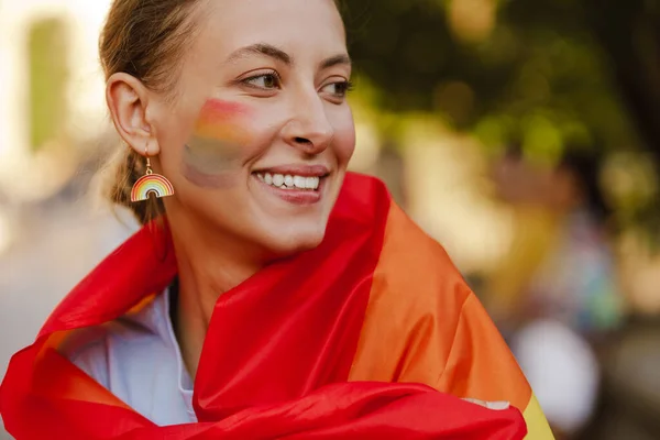 在城市街道上举行的骄傲阅兵式上 身穿彩虹旗的年轻女同性恋者面带微笑 — 图库照片