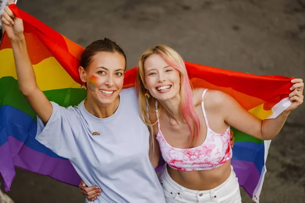 若いレズビアンカップル歩くとともに虹旗中にプライドパレードで街の通り — ストック写真