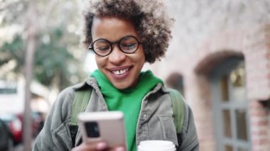 Yeşil kapüşonlu giyen gülen Afrikalı kadın dışarıda telefonla mesajlaşıyor.