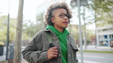 Yeşil kapüşonlu ciddi bir Afrikalı kadın sırt çantasıyla dışarı çıkıyor.