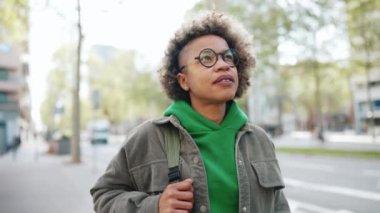 Yeşil kapüşonlu, kendine güvenen Afrikalı kadın dışarıda sırt çantasıyla dolaşıyor.