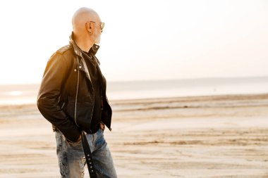 Siyah deri giyen cesur adam dışarıda poz verirken yan bakıyor.