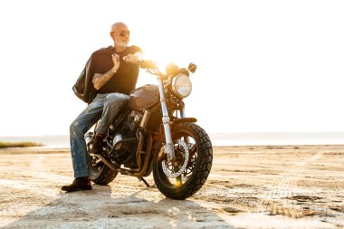 Yaz günü motosikletle dışarıda poz veren, dövmeli cesur bir adam.