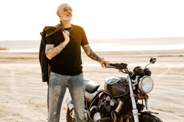 Güneş gözlüklü cesur adam yaz günü motosikletle dışarıda poz veriyor.