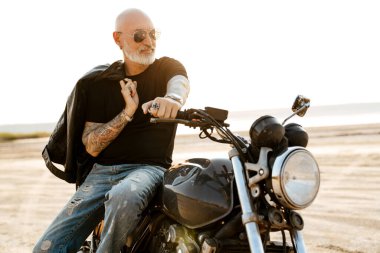 Yaz günü motosikletle dışarıda poz veren, dövmeli cesur bir adam.