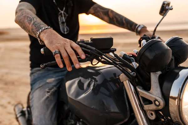 Mature man wearing black t-shirt with tattoo posing on motorbike outdoors