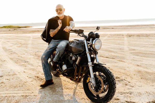 Yaz günü motosikletle dışarıda poz veren, dövmeli cesur bir adam.