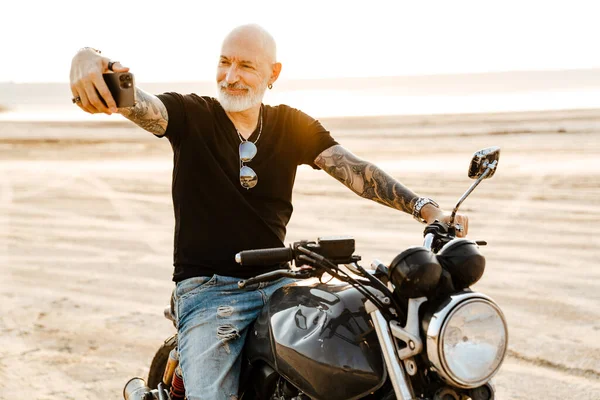 Mature Bold Man Taking Selfie Cellphone While Sitting Motorbike Outdoors — стоковое фото