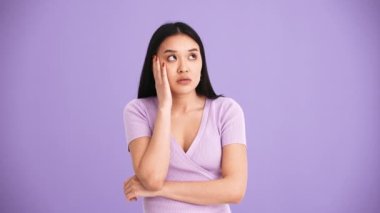 Mor tişört giyen Asyalı yorgun esmer kadın mor stüdyoda kameraya doğru esniyor.