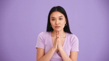 Mor tişört giyen üzgün Asyalı esmer kadın mor stüdyoda kameraya el çırpıyor.
