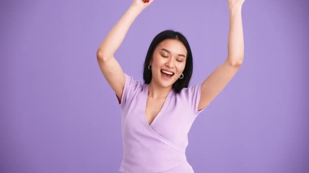 在紫色演播室里 身穿紫色T恤跳舞的亚洲黑发女子欢欣雀跃 — 图库视频影像