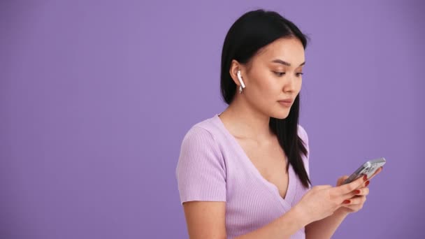 Positiva Mujer Morena Asiática Auriculares Escribiendo Por Teléfono Estudio Púrpura — Vídeo de stock