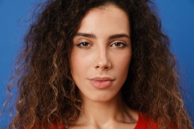 Genç esmer kadın poz veriyor ve mavi duvarın üzerinde izole edilmiş kameraya bakıyor.