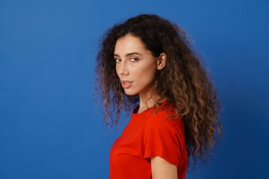 Genç esmer kadın poz veriyor ve mavi duvarın üzerinde izole edilmiş kameraya bakıyor.