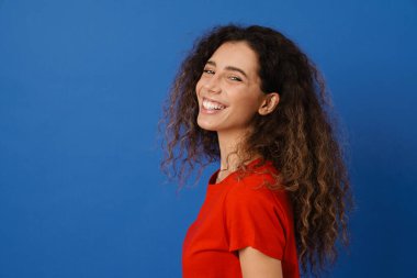 Genç esmer kadın gülümsüyor ve mavi duvarın üzerinden izole edilmiş kameraya bakıyor.