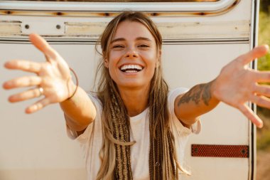 Beyaz, genç bir kadın gülümsüyor ve avuçlarını kameraya çeviriyor.