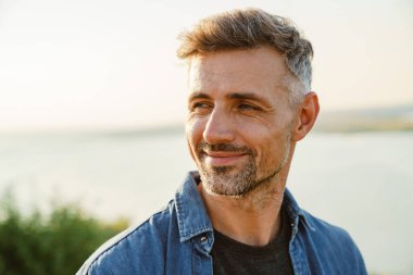 Gri Avrupalı adam dışarıda beklerken gülümsüyor ve yan bakıyor.