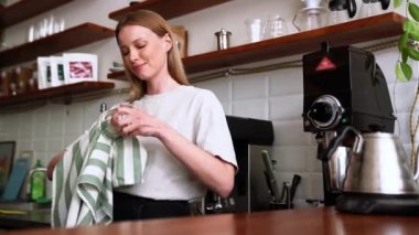 Yakışıklı sarışın kadın kafeteryadaki bardağı siliyor.