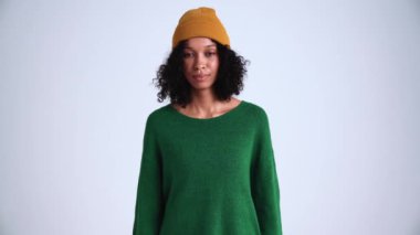 Gri stüdyodaki kameraya bakan, kendine güvenen kıvırcık saçlı bir kadın.