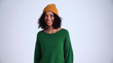 Gülen kıvırcık saçlı kadın gri stüdyoda kameraya bakıyor.