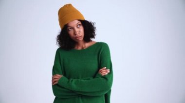 Kıvırcık saçlı yorgun kadın gri stüdyoda bir şey düşünüyor.