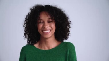 Neşeli kıvırcık saçlı kadın gri stüdyodaki kameraya bakıyor.