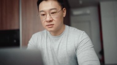 Evde dizüstü bilgisayarda yazan gözlüklü Asyalı mutlu adam.