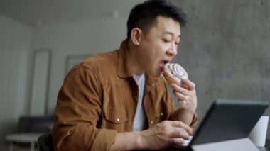Yakışıklı Asyalı adam evde çörek yiyor ve tabletten video seyrediyor.