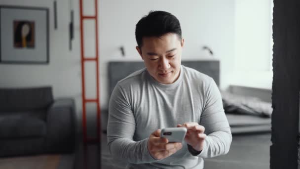 可愛いアジア人男性家で電話でテキストメッセージ — ストック動画