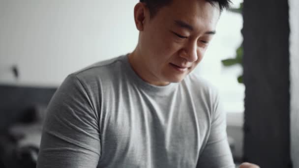 アジア人の笑顔男は自宅で電話で入力 — ストック動画