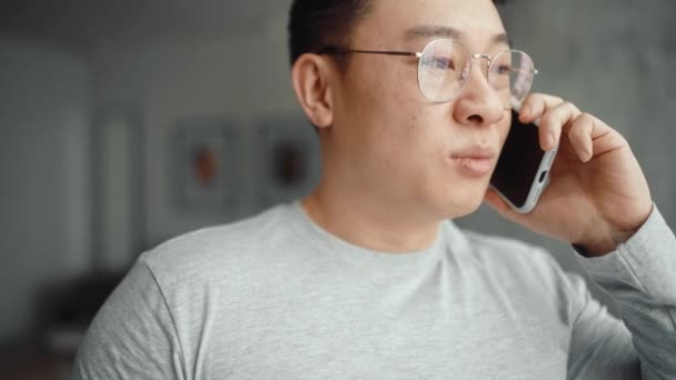 Vrolijke Aziatische Man Het Dragen Van Bril Praten Mobiele Thuis — Stockvideo