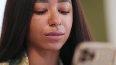 Pijama giyen kendine güvenen Afrikalı kadın cep telefonuyla mesaj atıyor.