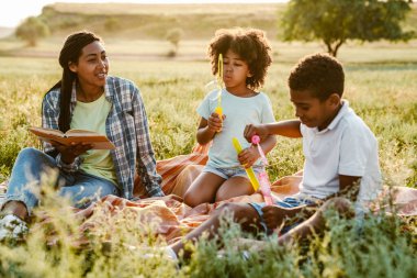 Siyah mutlu anne yaz tarlasında piknik yaparken iki oğluyla dinleniyor.
