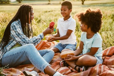 Siyah mutlu aile yaz tarlasında piknik yaparken sosisli yiyor.