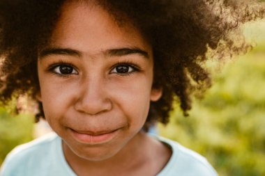 Siyah kıvırcık tişört giyen, gülümseyen ve dışarıdaki kameraya bakan çocuk.
