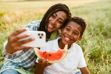 Siyah anne piknik sırasında oğluyla cep telefonunda fotoğraf çekiyor.