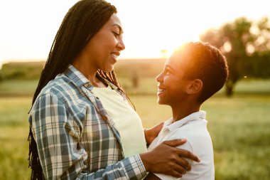 Siyah anne oğlunu kucaklıyor ve yaz tarlasında gülümsüyor.
