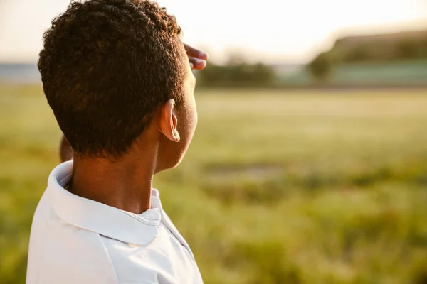 穿着白衬衫的黑人男孩站在夏天的田里看着日落 — 图库照片